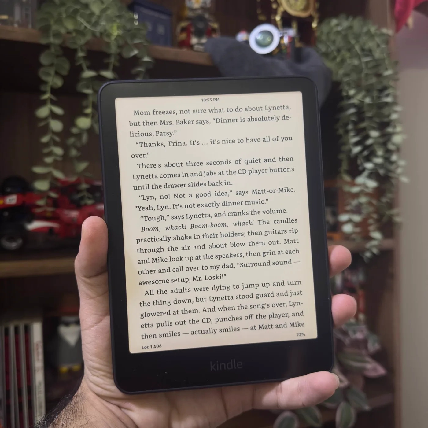 My Kindle Paperwhite held in one hand in front of my bookshelf.